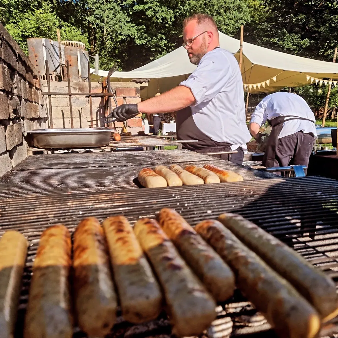 Koch beim Grillen von Bratwürsten am offenen Grill