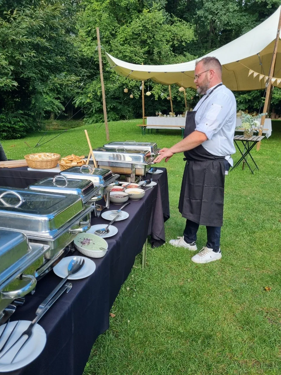 Koch richtet ein Cateringbuffet unter einem Zeltdach im Grünen an
