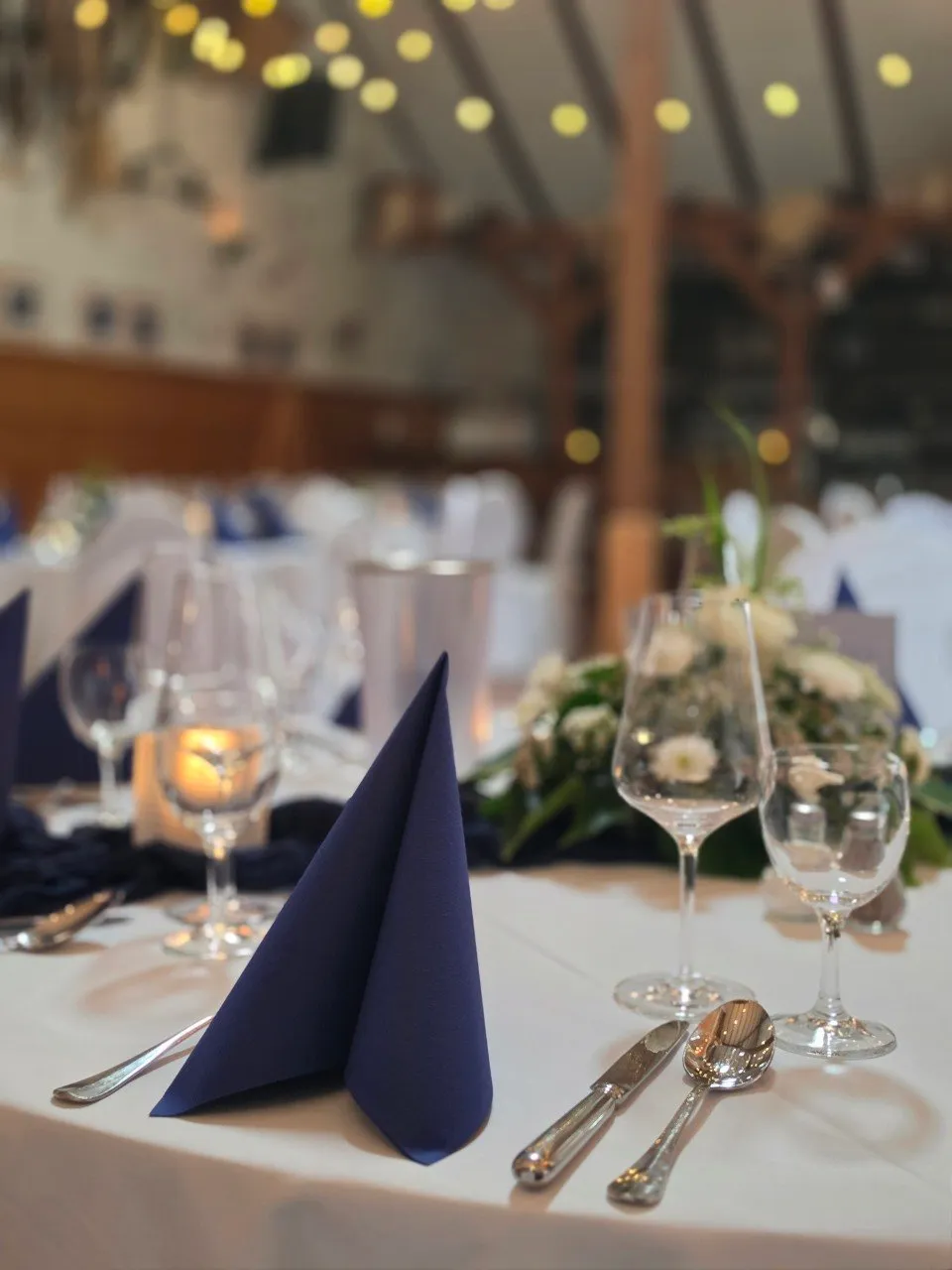 Blaue Serviette, Gläser und Blumenschmuck auf einer Hochzeitstafel