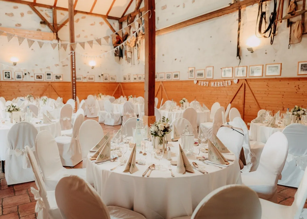 Festlich gedeckte Scheune mit runden Tischen und Just-Married-Dekoration
